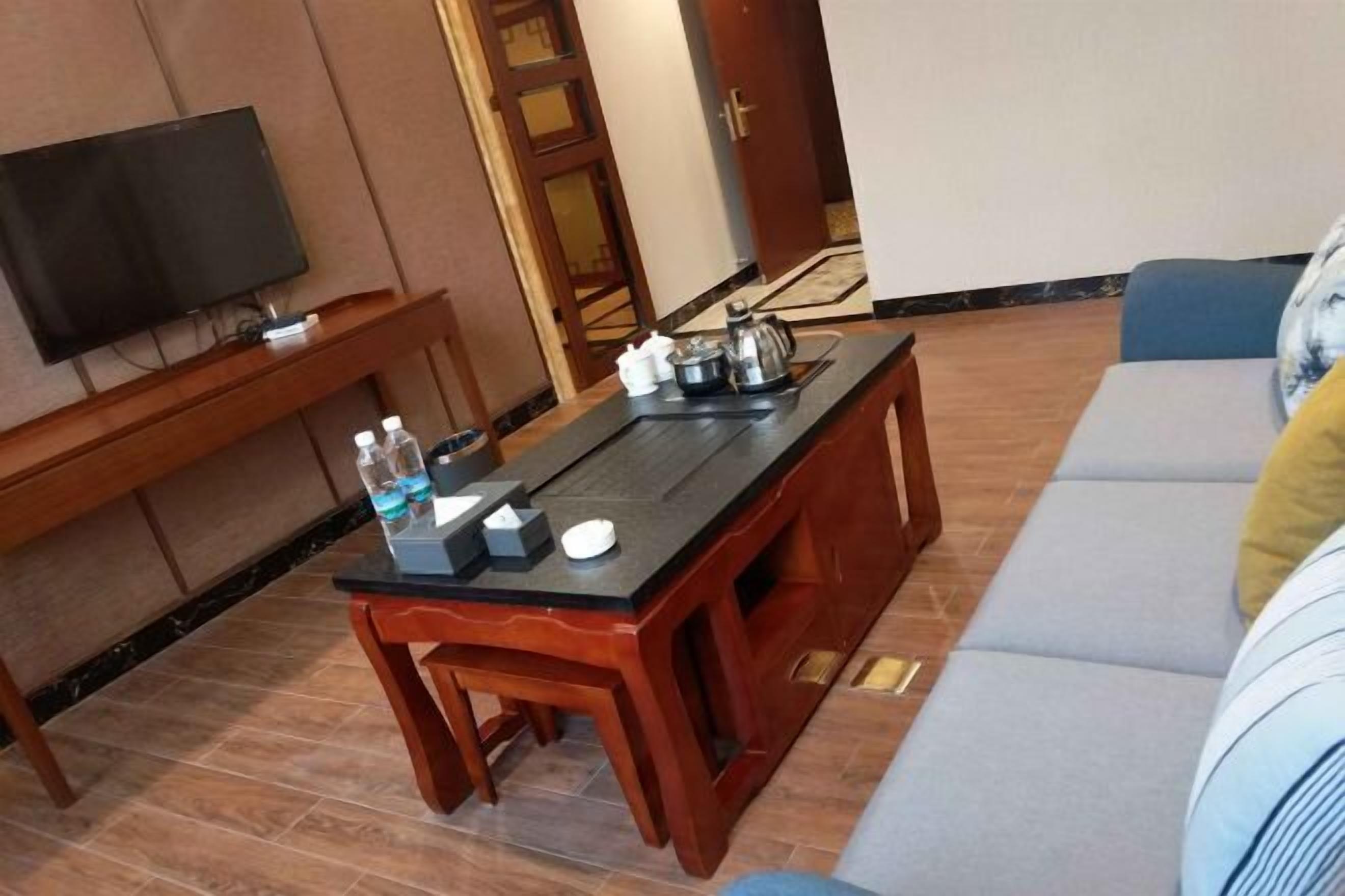 A living room with a TV, wooden furniture, a sofa, and a coffee table with items on it.