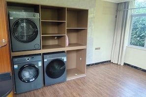 A laundry room with two washing machines and a drying rack, wooden shelving, and a large window with curtains. - Bishui Lantian Hotel (Funing)