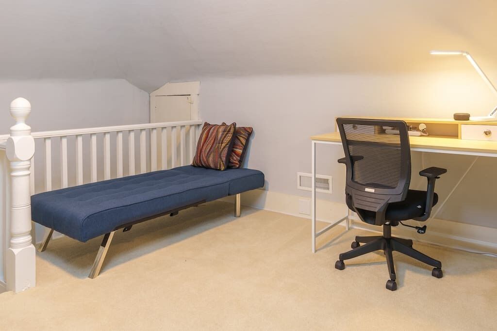 Quarto com cama azul, radiador branco, escrivaninha com cadeira e uma luminária.