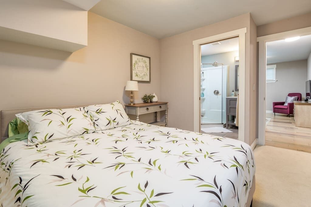 Une chambre à coucher comprenant un lit, une table de chevet, une lampe et une porte donnant sur une salle de bain.