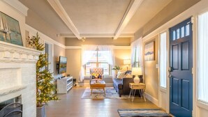 A spacious living room with a fireplace, a sofa, a coffee table, and a chair. There is a blue door on the right and a window with curtains on the left. - Upgraded Home with 5BR/4Bath/4 FREE gated parking/EV Charger (Seattle)