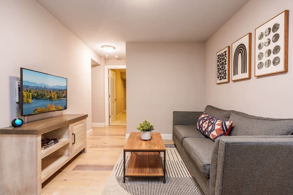 A modern living room with a flat-screen TV, a wooden coffee table, a gray sofa, and framed artwork on the wall.