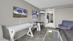 Una sala de estar moderna con una mesa blanca, sofá gris y televisor montado en la pared.