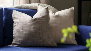 A blue sofa with two pillows, a window with curtains, and a painting on the wall.