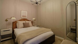 A bedroom with a bed, bedside tables, a nightstand, a mirror, and a ceiling light fixture.
