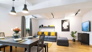 Ein modernes Wohnzimmer mit Essbereich, einem Sofa mit gelben Kissen, einer Deutschlandkarte an der Wand und einem Fernseher auf einem Schrank.