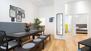 A modern, well-lit room with a wooden dining table, benches, and a small black table. There are framed pictures on the wall and a potted plant on the table.