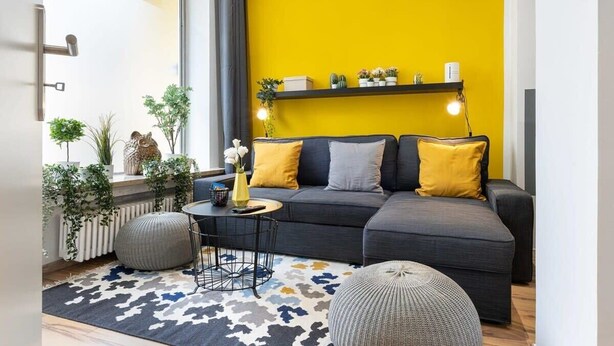 A modern living room with a grey sofa, yellow cushions, a round coffee table, and a patterned rug.