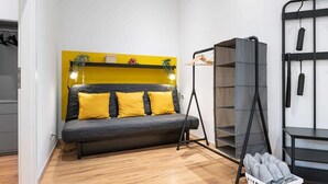 A compact living space with a sofa, a small table, a shelving unit, and a hanging rack.