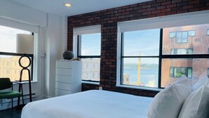 A hotel room with a large bed, a dresser, a chair, and a view of a building and water through two windows. - Reside Seattle Downtown, a Wyndham Residence (Seattle)