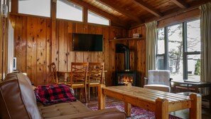 Ein gemütliches Blockhaus mit Holzvertäfelung, Kamin, Fernseher und Blick ins Freie.