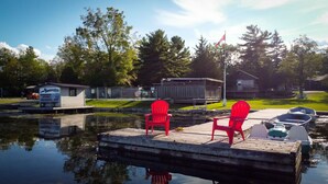 Un muelle con dos sillas rojas, una pequeña cabaña con el rótulo 'Sunnylea Housekeeping Cottages' y un asta con una bandera.