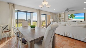 A spacious living area with a dining table, chairs, a sofa, and a television. - Capistrano E101. Gulf Front, Direct private beach access, Pet Friendly. (Seacrest)