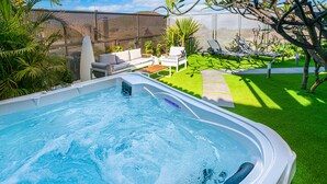 Piscina com hidromassagem, cercada por um jardim pequeno e mobiliário de exterior.
