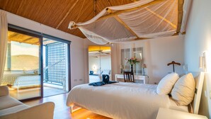 Quarto com uma cama grande, escrivaninha, cadeira e varanda com vista para a praia.