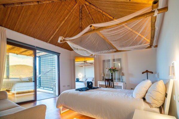 Un dormitorio con una cama grande, un escritorio, una silla y un balcón con vistas a la playa.