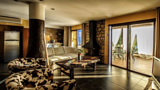 Uma sala de estar ampla com lareira de pedra, um sofá e um espaço de jantar com mesa e cadeiras.