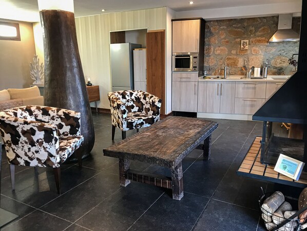 Una sala de estar moderna con una mesa de centro de madera, dos sillones estampados, un pilar oscuro y una pared de piedra.