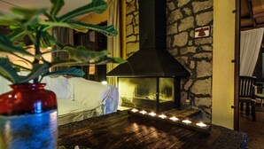 Um quarto acolhedor com lareira de pedra, uma mesa de madeira com velas e um vaso de planta.