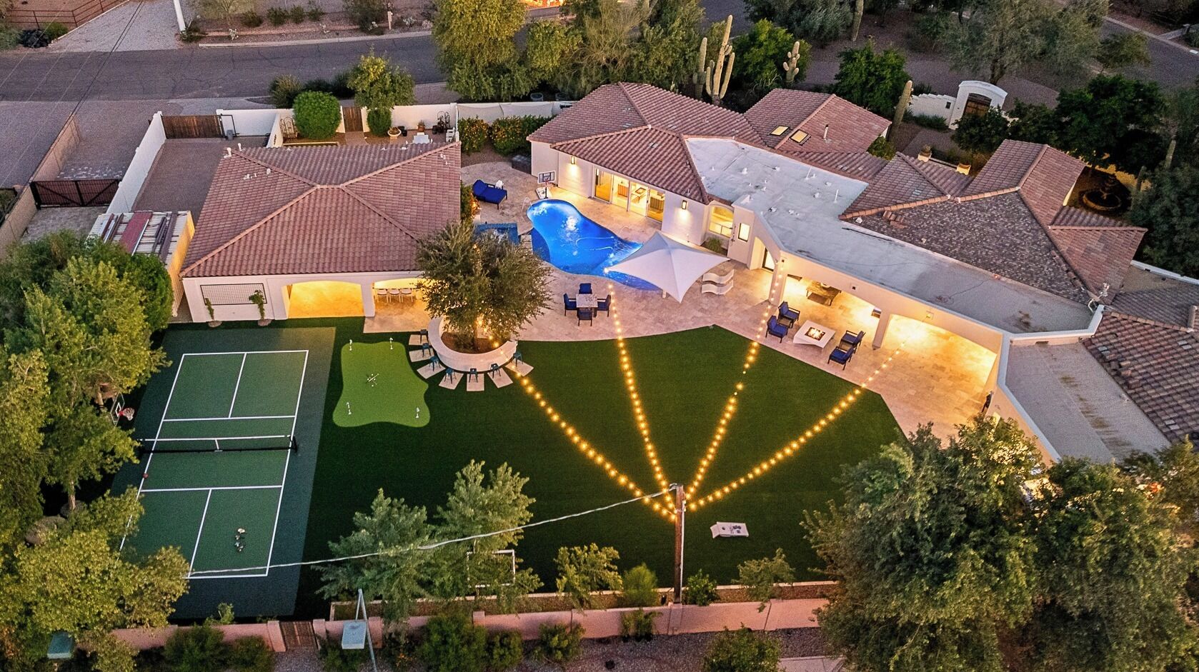 An aerial view of a residential property with a swimming pool, tennis court, and landscaped garden.