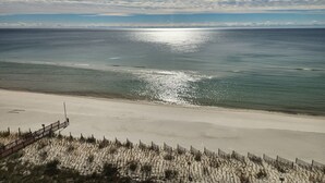 Ein Strand mit einem Zaun und Vegetation im Vordergrund, mit freiem Blick auf das Meer und den Himmel.