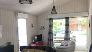 Un soggiorno ampio con pavimento in legno, un divano giallo, una poltrona bianca e un tavolino blu. Due lampade a sospensione nere pendono dal soffitto.