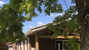 Un rustico chalet in legno con un portico coperto, una strada d'accesso sterrata e una recinzione in legno.