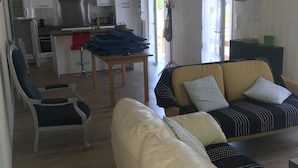 Un soggiorno moderno con un divano, una poltrona e un tavolo da pranzo. È presente un angolo cottura con mobili bianchi e un fornello.