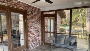 A room with a brick wall, large sliding glass doors, a ceiling fan, and a wooden deck with a bench.