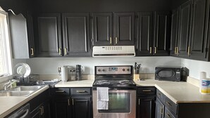 A modern kitchen with dark cabinets, stainless steel appliances, and a wooden floor.