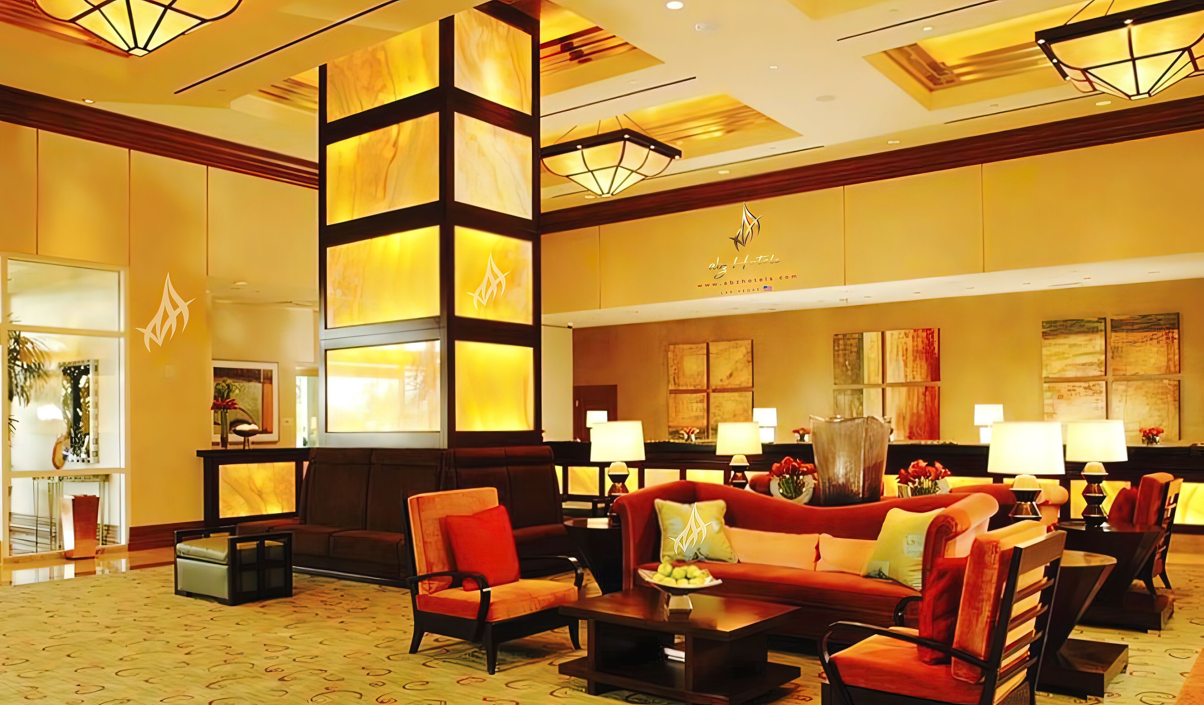 A hotel lobby with a central seating area, a reception desk, and artwork on the walls.