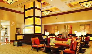 A hotel lobby with a central seating area, a reception desk, and artwork on the walls.