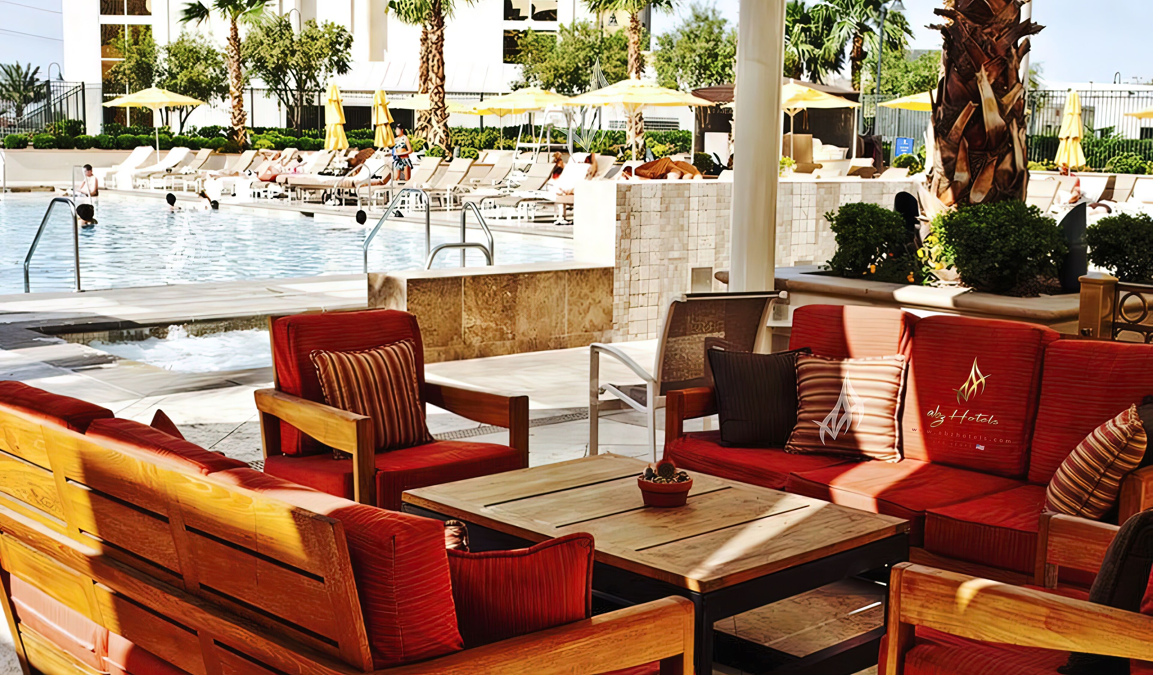 A poolside area with lounge chairs, a wooden table, and a bar area.