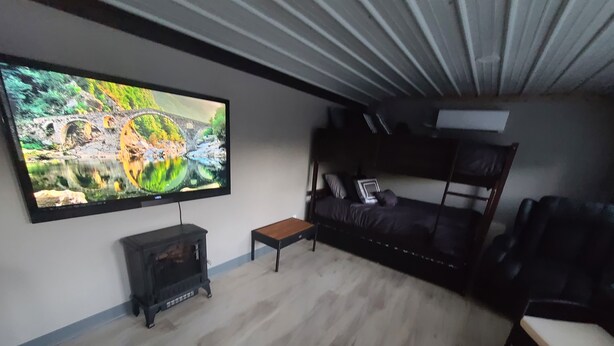A modern living room with a flat-screen TV, a sofa, a wooden coffee table, and a black leather armchair. - Cabin 1 at the Pallet Factory (Leadwood)