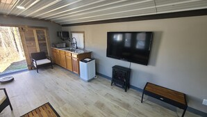 A spacious living area with a kitchen, a large flat-screen TV mounted on the wall, a built-in stove, and a bench. - Cabin 1 at the Pallet Factory (Leadwood)