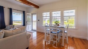 A room with a wooden floor, white walls, a dining table with chairs, a sofa, and large windows with a view of greenery and a building. - Miramar Escape (North Hampton)