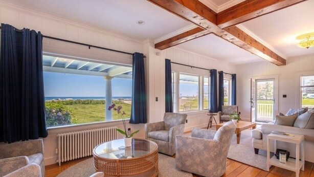 A spacious living room with a view of the sea, featuring a round coffee table, comfortable seating, and a wooden ceiling. - Miramar Escape (North Hampton)