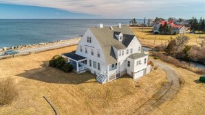 A large white house with a green roof, a covered porch, and a small attached garage, located near a body of water and a road. - Miramar Escape (North Hampton)