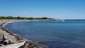 A coastal landscape with a rocky shoreline, calm sea, and a distant shoreline with buildings and vegetation. - Miramar Escape (North Hampton)