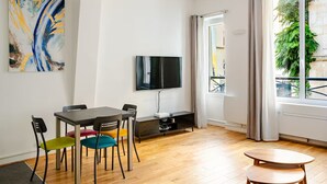 Un soggiorno moderno con zona pranzo, televisione a schermo piatto montata a parete e un'ampia finestra con tende.