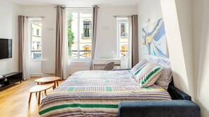 Una camera da letto con un letto, una scrivania, una sedia, una TV e una finestra con tende.