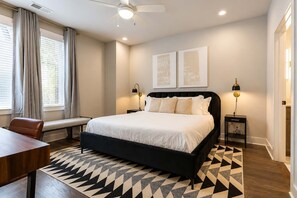 A modern bedroom with a large bed, bedside lamps, a bench, and a geometric-patterned rug.
