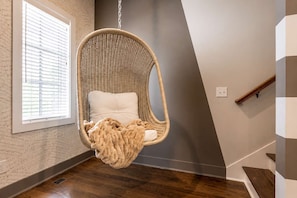 Un fauteuil suspendu avec un coussin et une couverture, dans une pièce dotée d’une fenêtre et d’un escalier.
