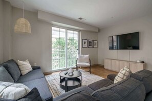 A modern living room with a grey sofa, a round coffee table, a white chair, and a TV mounted on the wall. - Downtown Luxury Apartment on the Columbus Commons (Columbus)