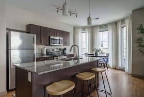 A modern kitchen with dark cabinets, stainless steel appliances, a granite countertop, and a bar area with stools. - Downtown Luxury Apartment on the Columbus Commons (Columbus)