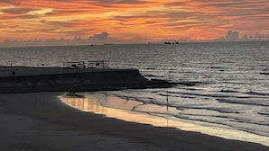 Rantamaisema auringonlaskun aikaan, tyyni meri ja kaupungin siluetti horisontissa.