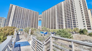 A high-rise hotel with multiple balconies, a wooden boardwalk, and a clear blue sky. - 5 Star Amenities at North Beach Resort Direct Ocean View Condo,Pools,Hot Tubs (North Myrtle Beach)