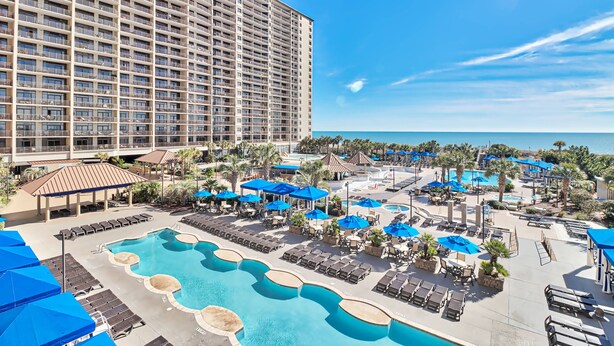 A hotel with a large pool area, multiple lounge chairs, and umbrellas. - 5 Star Amenities at North Beach Resort Direct Ocean View Condo,Pools,Hot Tubs (North Myrtle Beach)