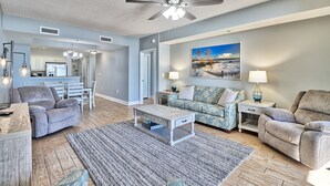 A spacious living room with a ceiling fan, a dining area, and a kitchen in the background. - 5 Star Amenities at North Beach Resort Direct Ocean View Condo,Pools,Hot Tubs (North Myrtle Beach)