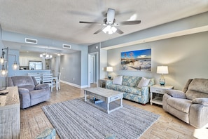 A spacious living room with a ceiling fan, a dining area, and a kitchen in the background.